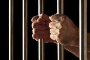 Close-up of a person’s hands gripping jail bars, symbolizing arrest and incarceration.