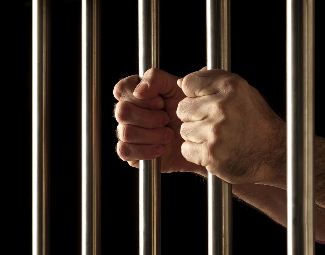 Close-up of a person’s hands gripping jail bars, symbolizing arrest and incarceration.