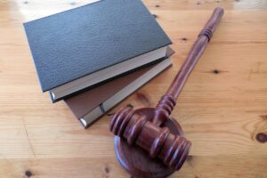 A wooden gavel resting on its block next to a stack of two law books on a light wooden table. Represents the legal implications and defense strategy for Texas gun and firearm charges.