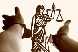 Silhouette of Lady Justice holding the scales, with two hands reaching from the sides against a light background.