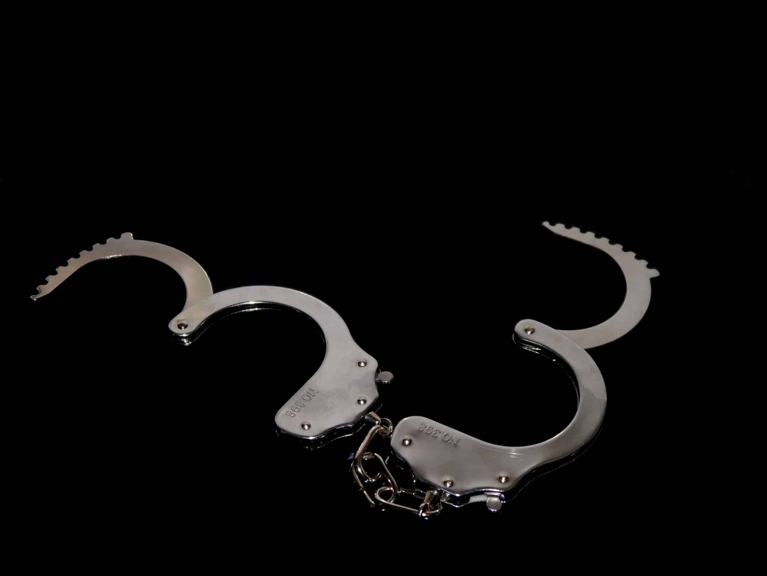 Close-up of silver handcuffs resting on a black surface.